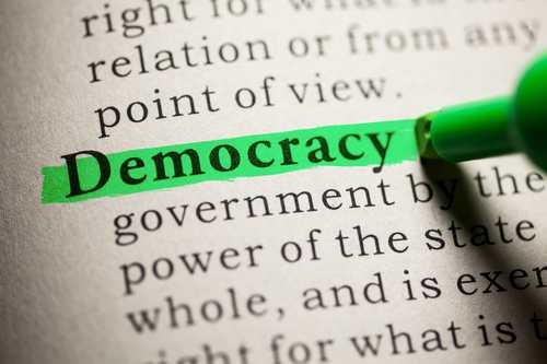 An open dictionary with a green marker highlighting the word democracy