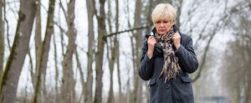 Lady pulling her collar up as she walks through the woods