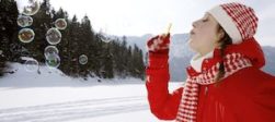 Get Outside - Lady in a red and white hat and scarf and red coat blowing bubbles with a snowy landscape behind her