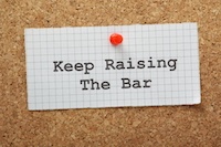 A note tacked to a corkboard with the words "keep raising the bar"